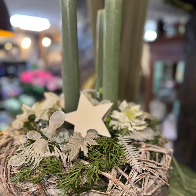 Adventskranz mit vier grünen Kerzen, dekoriert mit Tannenzweigen, weißen Blüten und einem weißen Stern aus Holz
