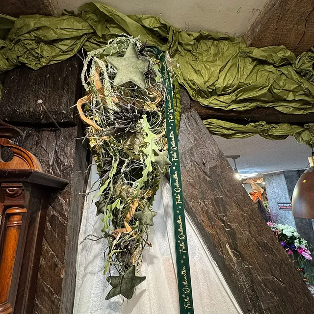 Hängender Weihnachtsstrauß mit Sternen, Zweigen, Blättern und grünem Band an einer Holzwand