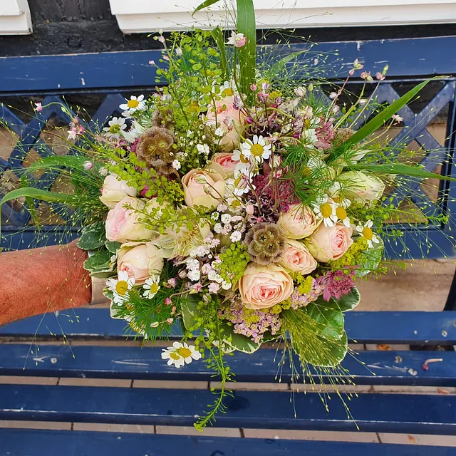 Bunter Blumenstrauß mit Rosen, Kamille und verschiedenen grünen Pflanzen auf einer blauen Holzbank