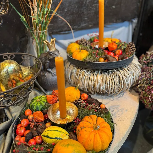 Herbstliche Tischdekoration mit kleinen Kürbissen, Kerzen, Beeren und einer Froschfigur mit Krone