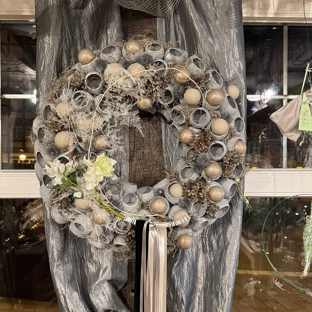 Weihnachtskranz mit goldfarbenen Kugeln, getrockneten Pflanzen und weißen Bändern vor silbernem Hintergrund