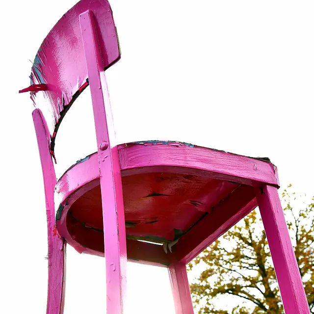 Nahaufnahme eines pinkfarbenen Holzstuhls von unten mit Baum im Hintergrund