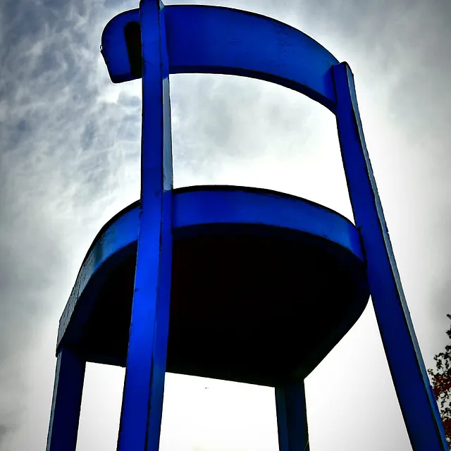 Blick von unten auf einen großen blauen Stuhl vor bewölktem Himmel
