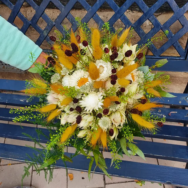Bunter Blumenstrauß mit weißen, gelben und dunkelroten Blüten sowie grünem Beiwerk auf einer blauen Holzbank